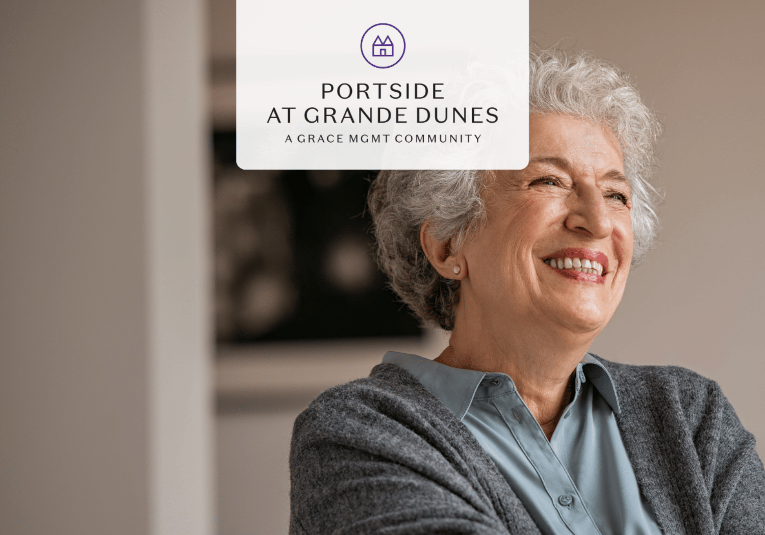 Cheerful elderly woman with gray hair in a blue blouse and gray cardigan; overlay badge reads Portside at Grande Dunes.