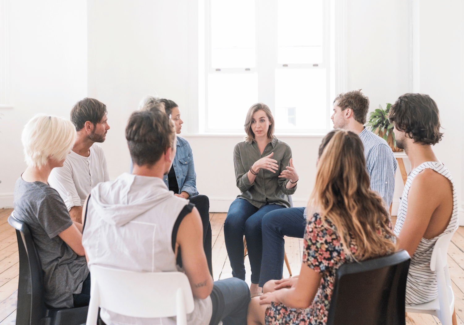 Group of adults seated in a circle, a woman in a green blouse speaks while others listen in a bright room.